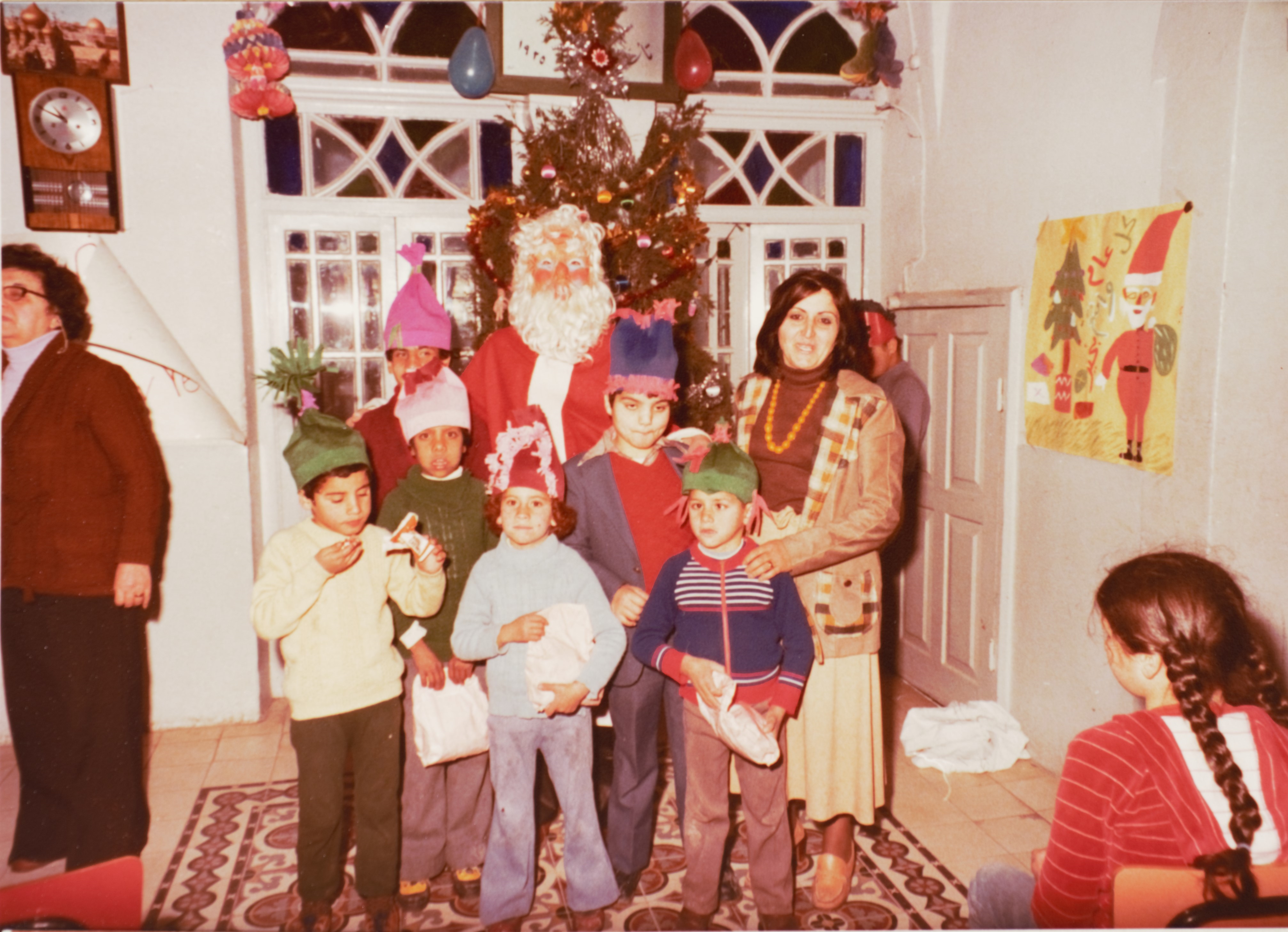 Colour photo of kids, a Santa in an mask, and a parent in front of a Christmas tree.
