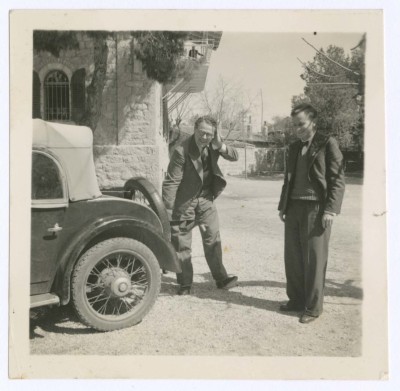 A Photograph of Two People Standing Behind an Old Car