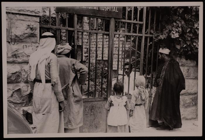 صورة لرجال وطفلين يقفون  أمام باب  إحدى المستشفيات، ثلاثينيات وعشرينيات القرن الماضي