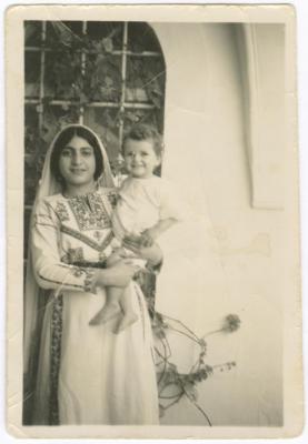  أسماء عرنكي تحملُ أحد أطفال العائلة في محيط بيتهم، بيزيت، 1948-1949 