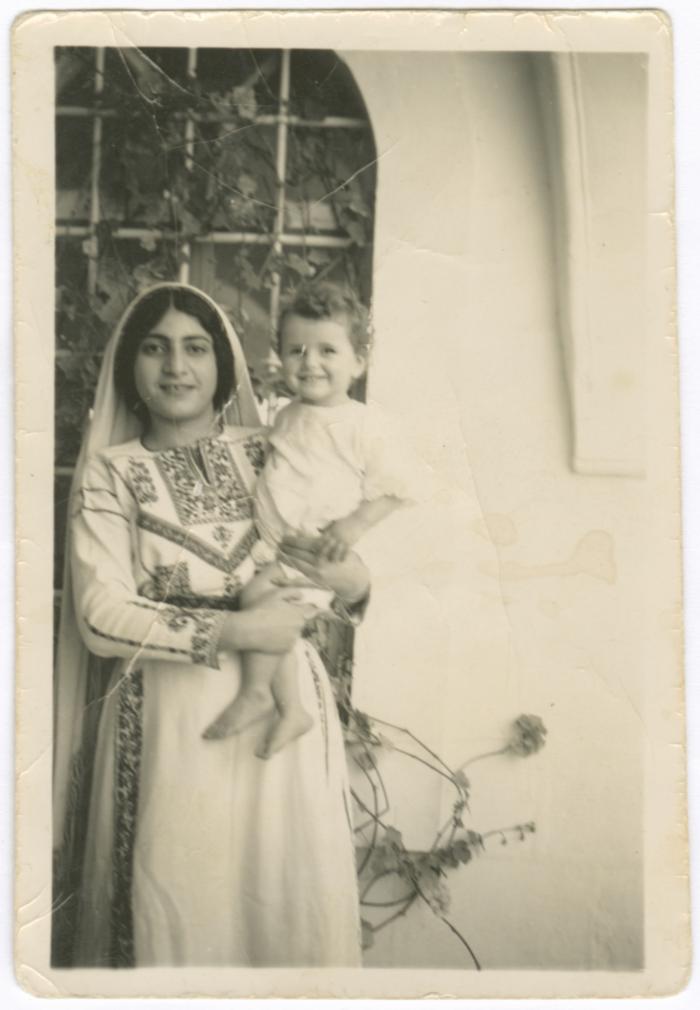  أسماء عرنكي تحملُ أحد أطفال العائلة في محيط بيتهم، بيزيت، 1948-1949 