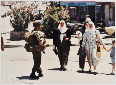 نساء فلسطينيات يعبرن دوار المنارة من أمام جنود الاحتلال الإسرائيلي، رام الله، تسعينيات القرن العشرين