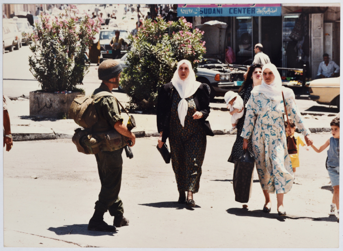 نساء فلسطينيات يعبرن دوار المنارة من أمام جنود الاحتلال الإسرائيلي، رام الله، تسعينيات القرن العشرين