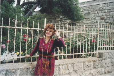 Maha El-Saca standing before her house in Beit Jala, wearing the traditional dress of Bayt Jibrin
